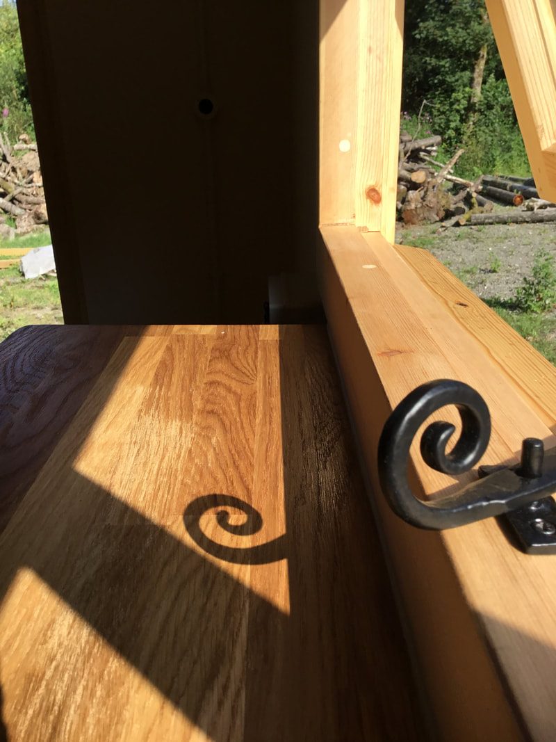 A hand-forged curled iron monkey-tail catch fitted to a timber window.