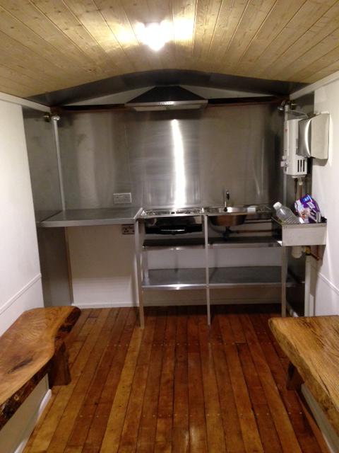 A compact stainless steel kitchen fitted into the end of a shepherd's hut.