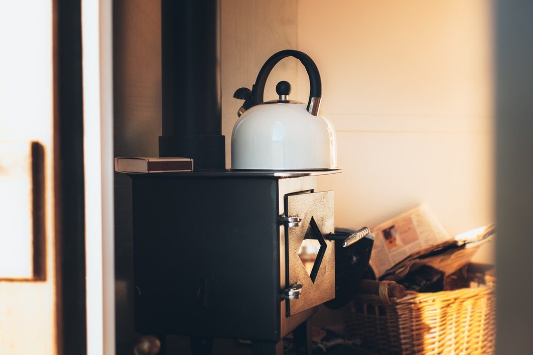 A small cast-iron wood-burning stove with a kettle on top, inside a hut.