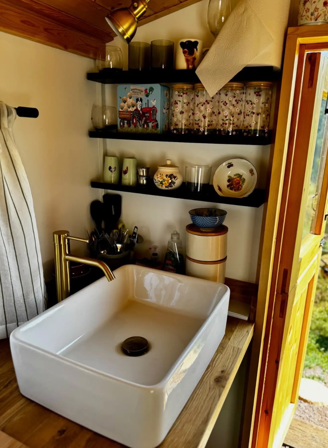 A kitchenette basin with a brass tap and open shelves inside a shepherd hut.